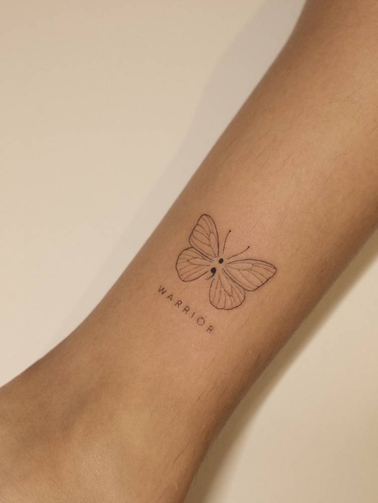 Semicolon butterfly and word "warrior" tattooed on the ankle.