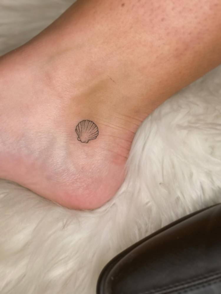 Scallop shell tattoo in fine line style located on the ankle.