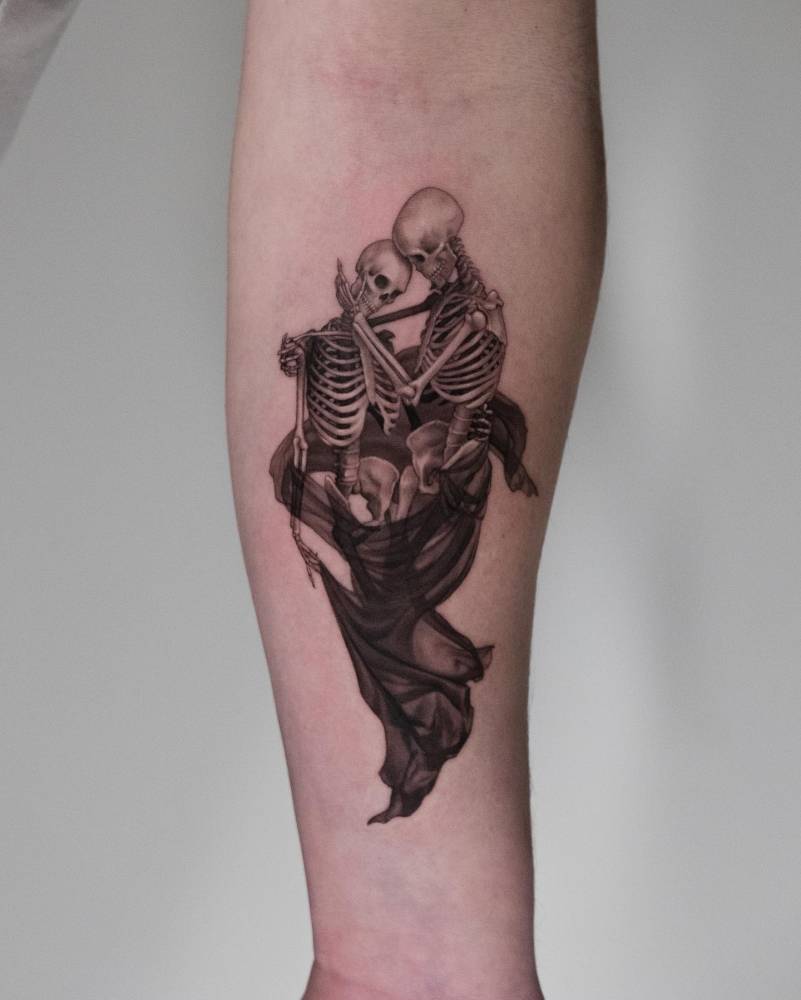 Skeletons hugging tattooed on the inner forearm.