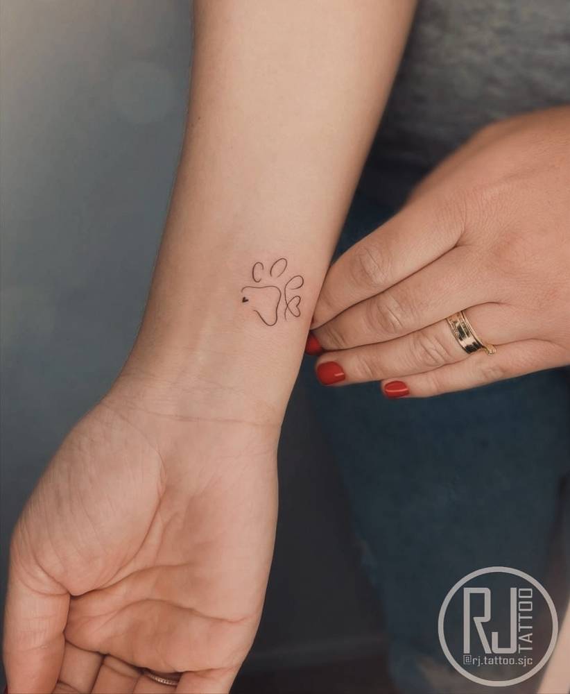 Fine line style dog paw print and heart tattoo located on the wrist.