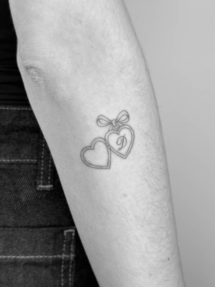 Heart pendant and initial "D" tattooed on the forearm.