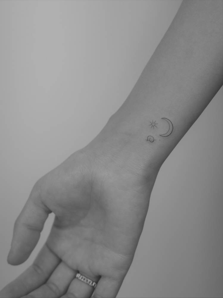 Crescent moon and sun tattooed on the wrist, minimalistic style.