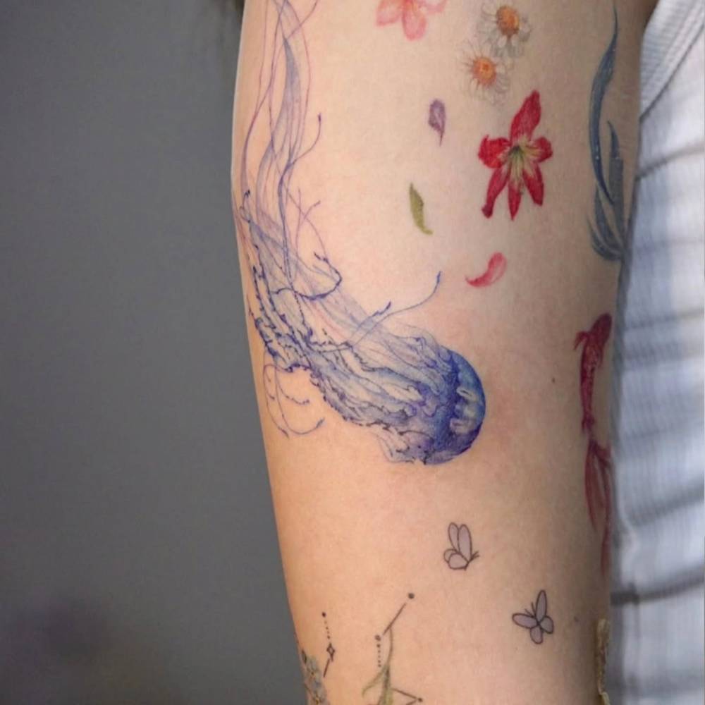 Jellyfish tattoo in watercolor style tattooed on the upper arm.