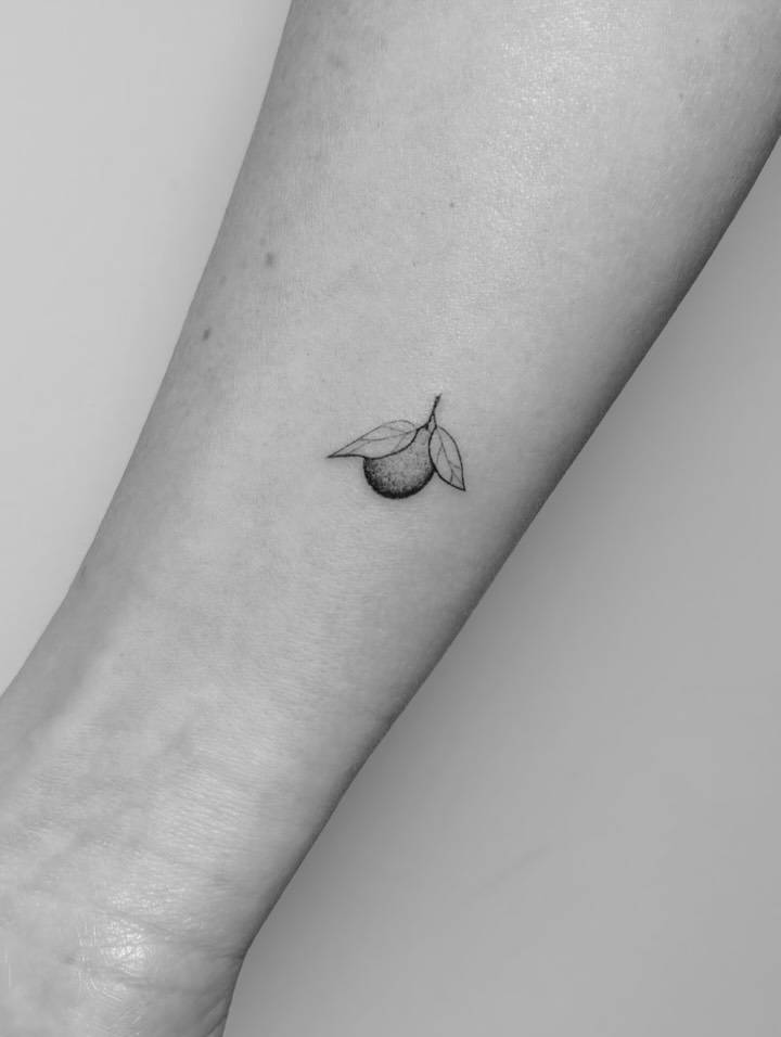 Tiny clementine tattoo in illustrative style located on the wrist.