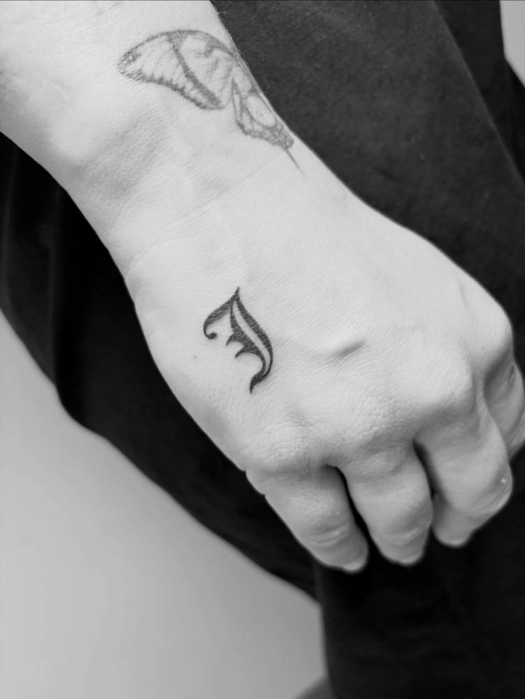 Letter "J" in gothic font tattooed on the hand.