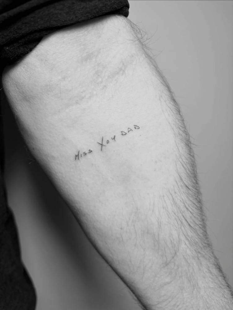 "Miss you, dad" lettering tattoo located on the inner forearm.