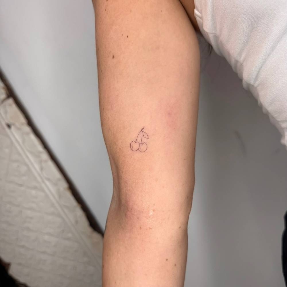 Tiny minimalistic cherry tattoo located on the inner arm.