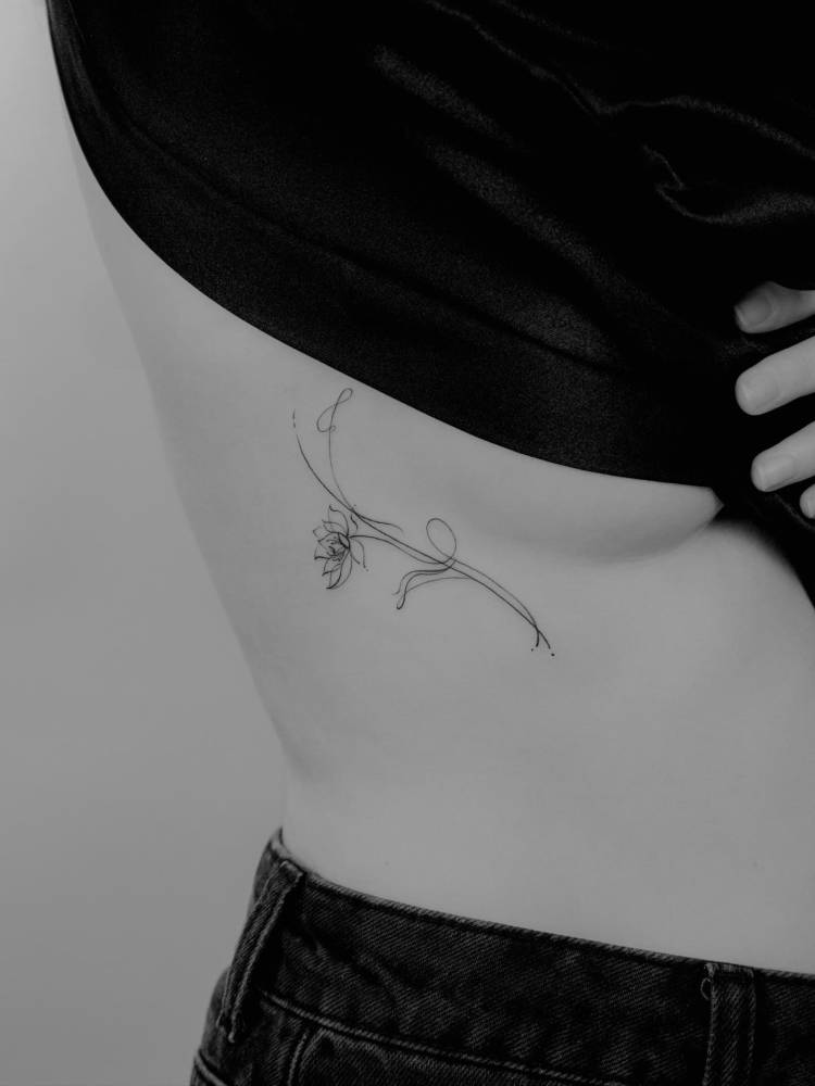 Lotus flower tattoo in fine line style located on the side boob.