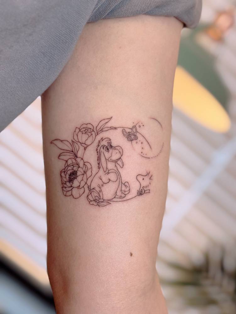 Eeyore and Woodstock tattoo in fine line style located on the inner arm.