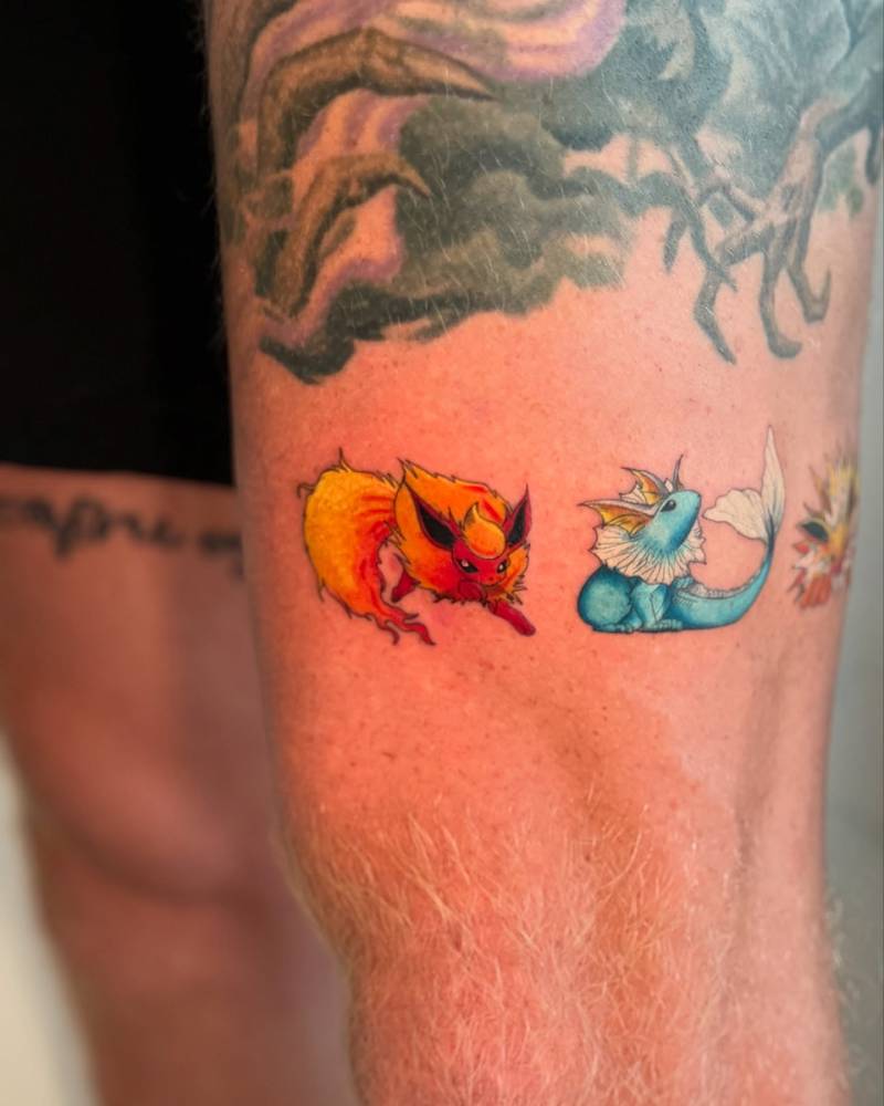 Flareon and Vaporeon tattoo located on the thigh, cartoon style.