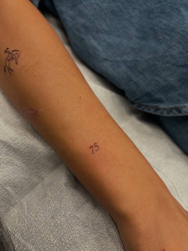 Little tattoo of the number "75" located on the wrist.