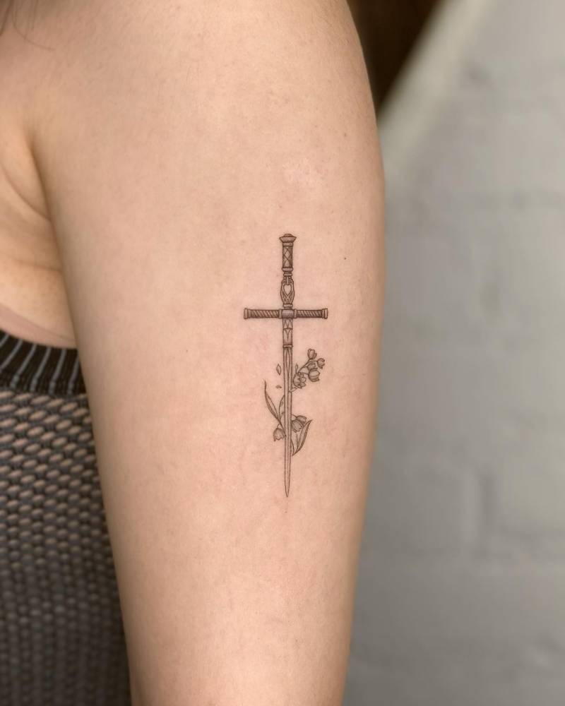 Swords and lily of the valley flowers tattooed on the upper arm.