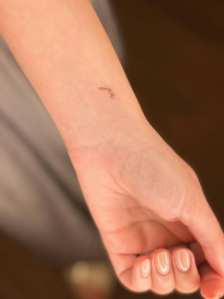 Word "pa" tattooed on the wrist in handwritten font.