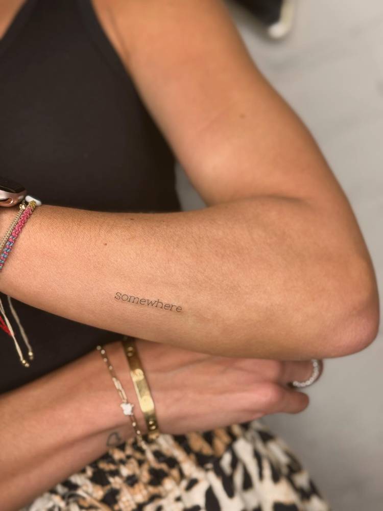 Typewriter font word "somewhere" tattooed on the forearm.