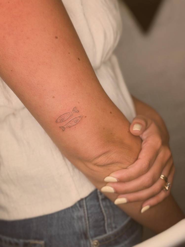 Two opposite fish tattoo in fine line style located on the tricep.