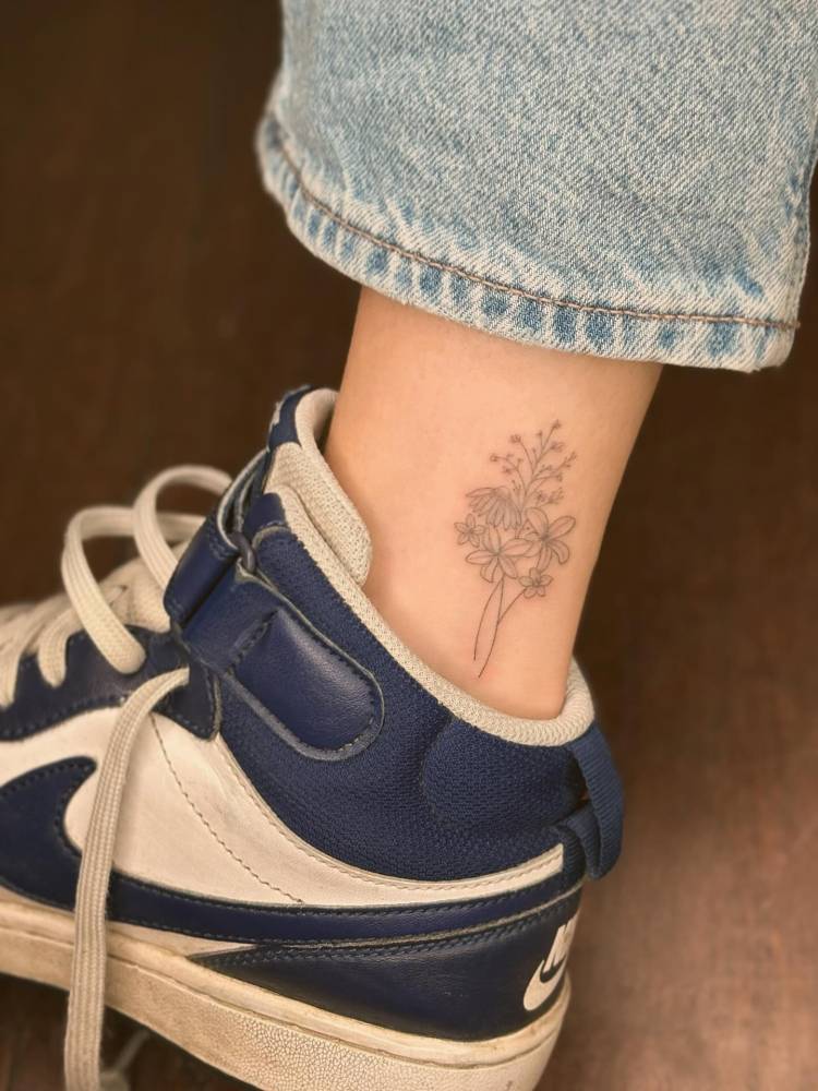 Fine line style flower bouquet tattoo done on the ankle.