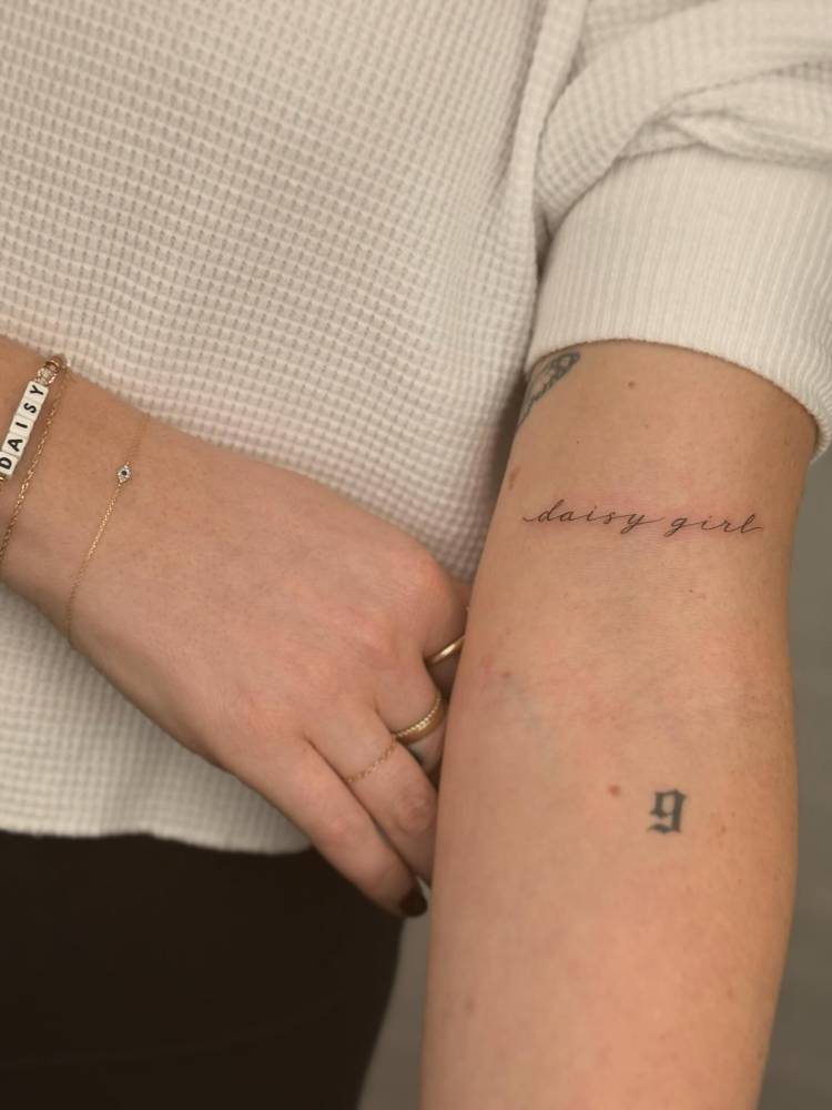 "Daisy girl" lettering tattoo located on the bicep.