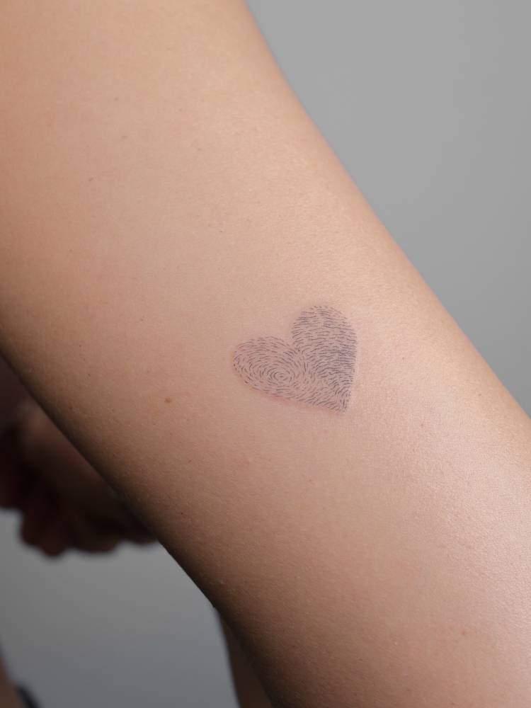 Fingerprint heart tattoo located on the tricep, fine line style.