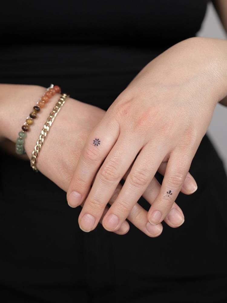 Minimalistic flower and ornament tattoos located on the fingers.
