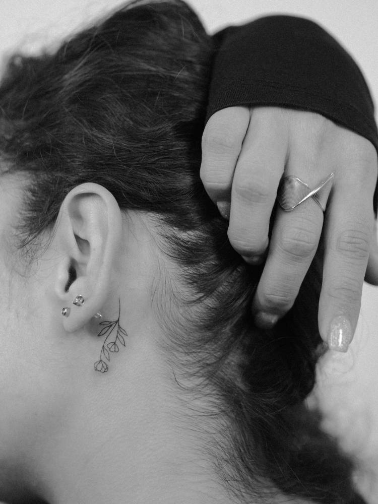Little flowers tattooed behind the ear, done in fine line style.