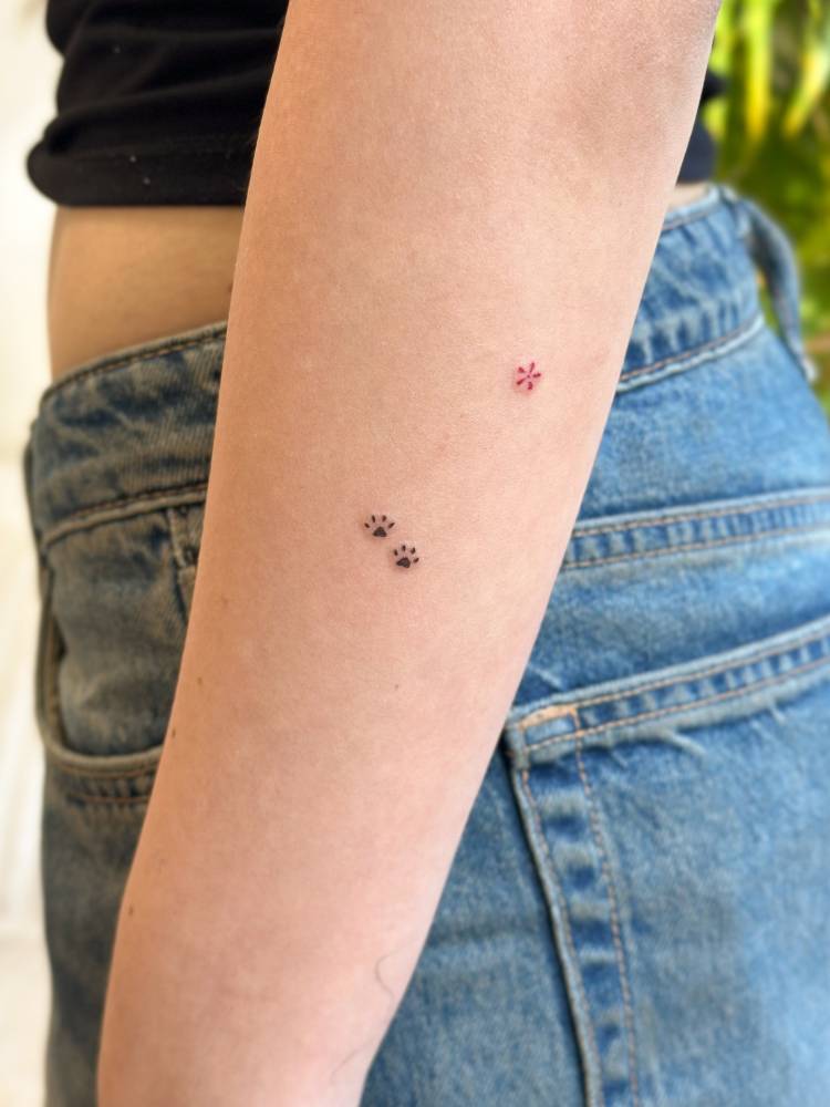 Tiny minimalistic paws print and red flower tattooed on the forearm.