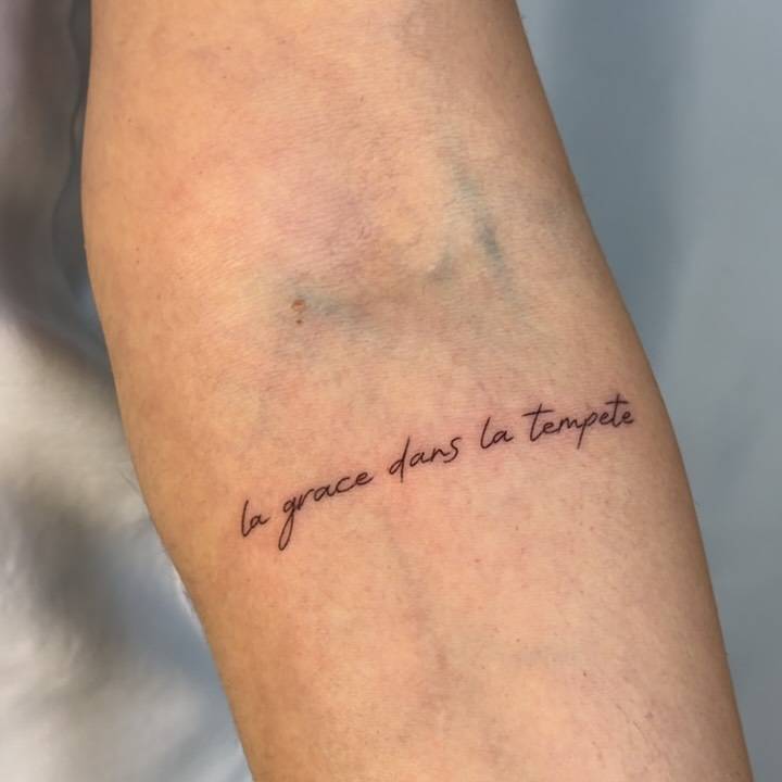 "La grace dans la tempete" lettering tattoo handwritten on the inner forearm.