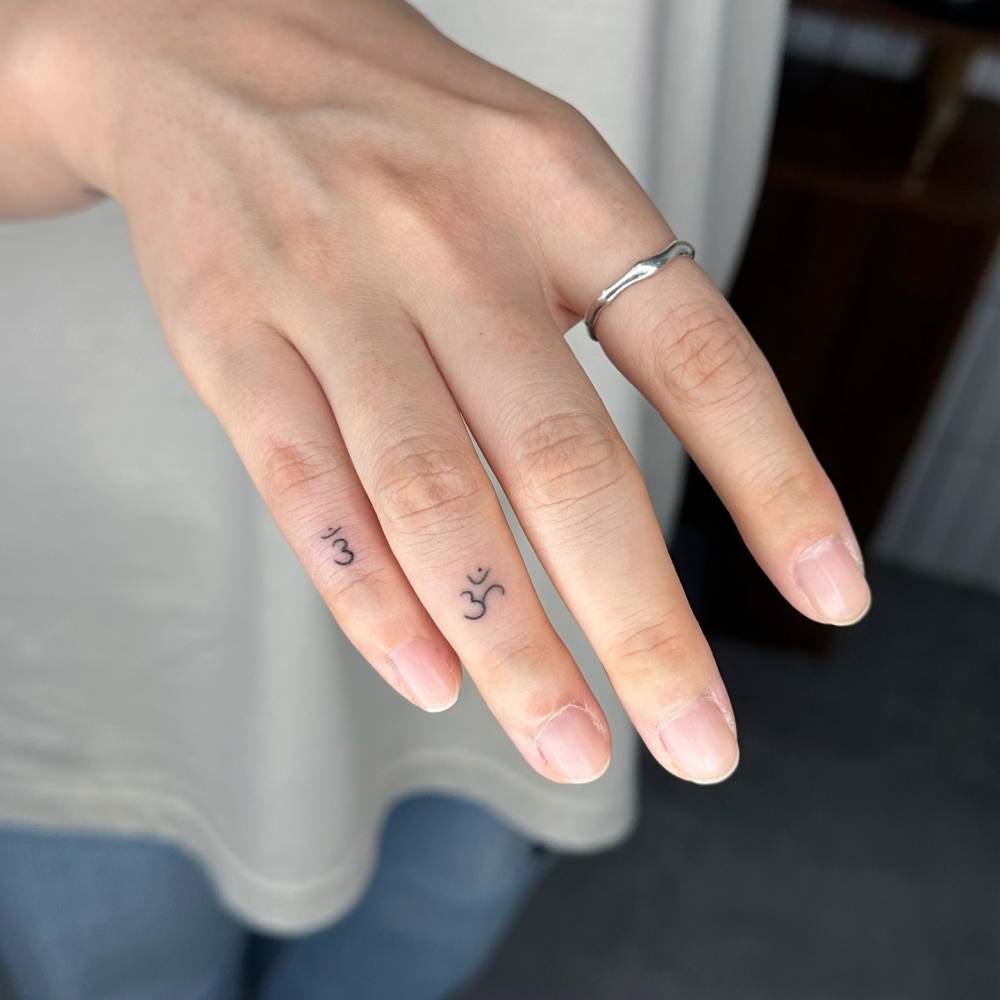 Om tattoos located on the fingers, minimalistic style.