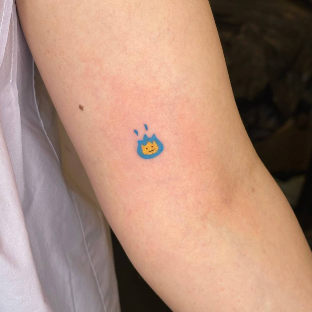 Blue fire tattoo in cartoon style located on the inner arm.