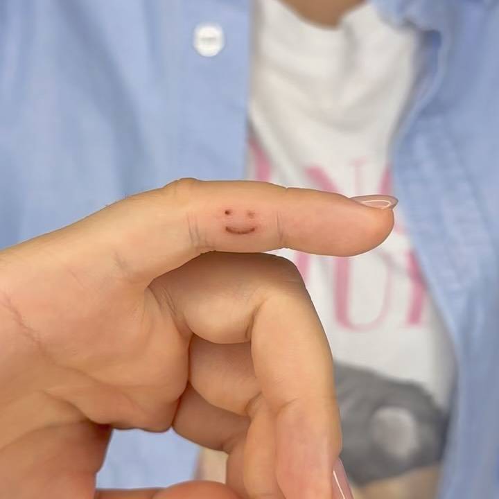 Smiley face birthmark cover up tattoo located on the finger.
