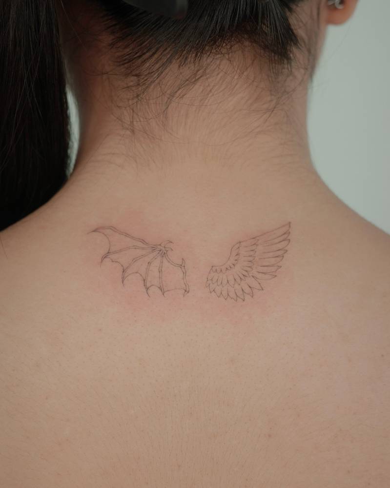 Devil and angel wings tattoo located on the upper back, fine line style.
