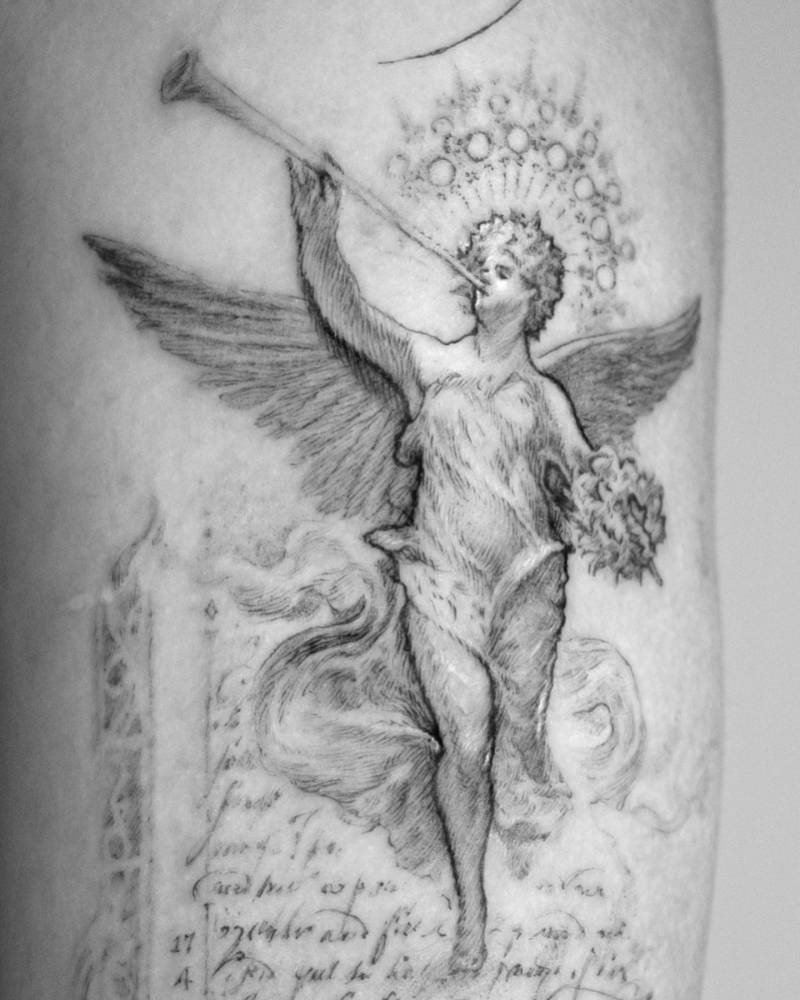 Angel playing the trumpet tattoo located on the upper arm.