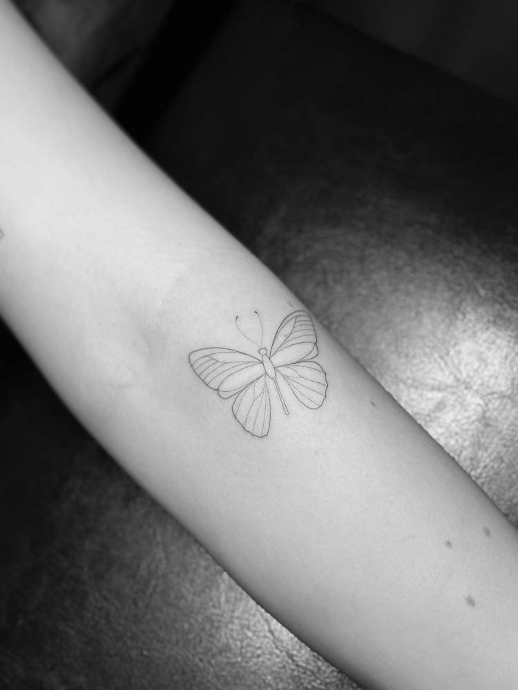 Little butterfly tattoo in fine line style located on the forearm.