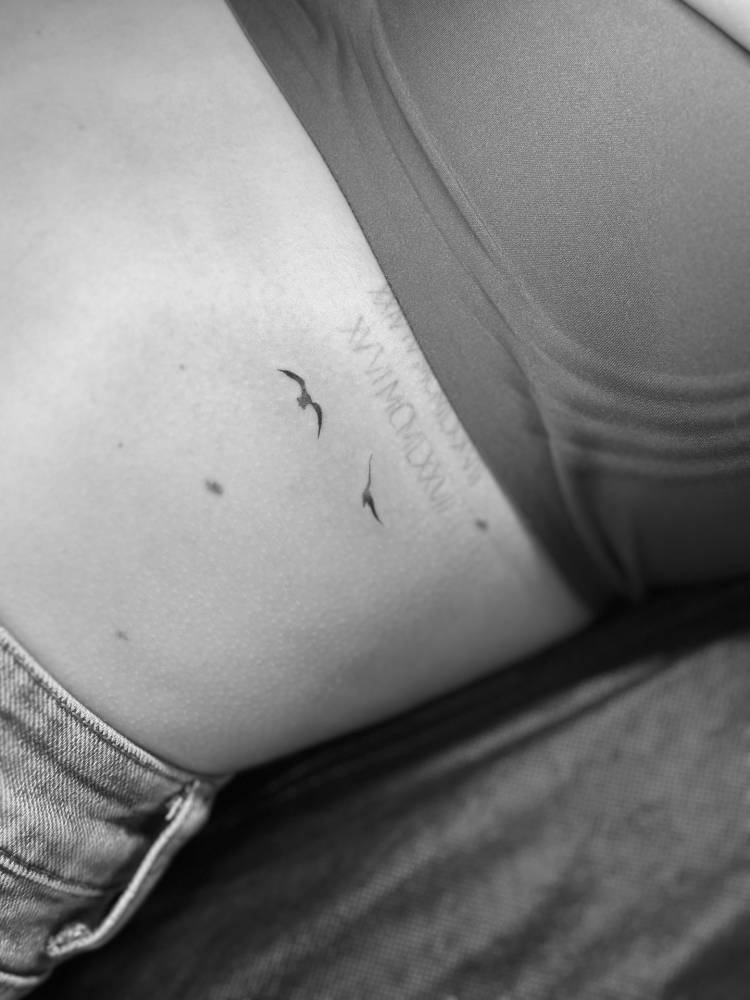 Minimalistic style flying birds tattoo placed on the rib.