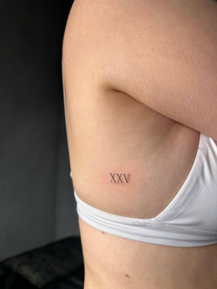 Roman numeral tattoo in serif font located on the side boob.