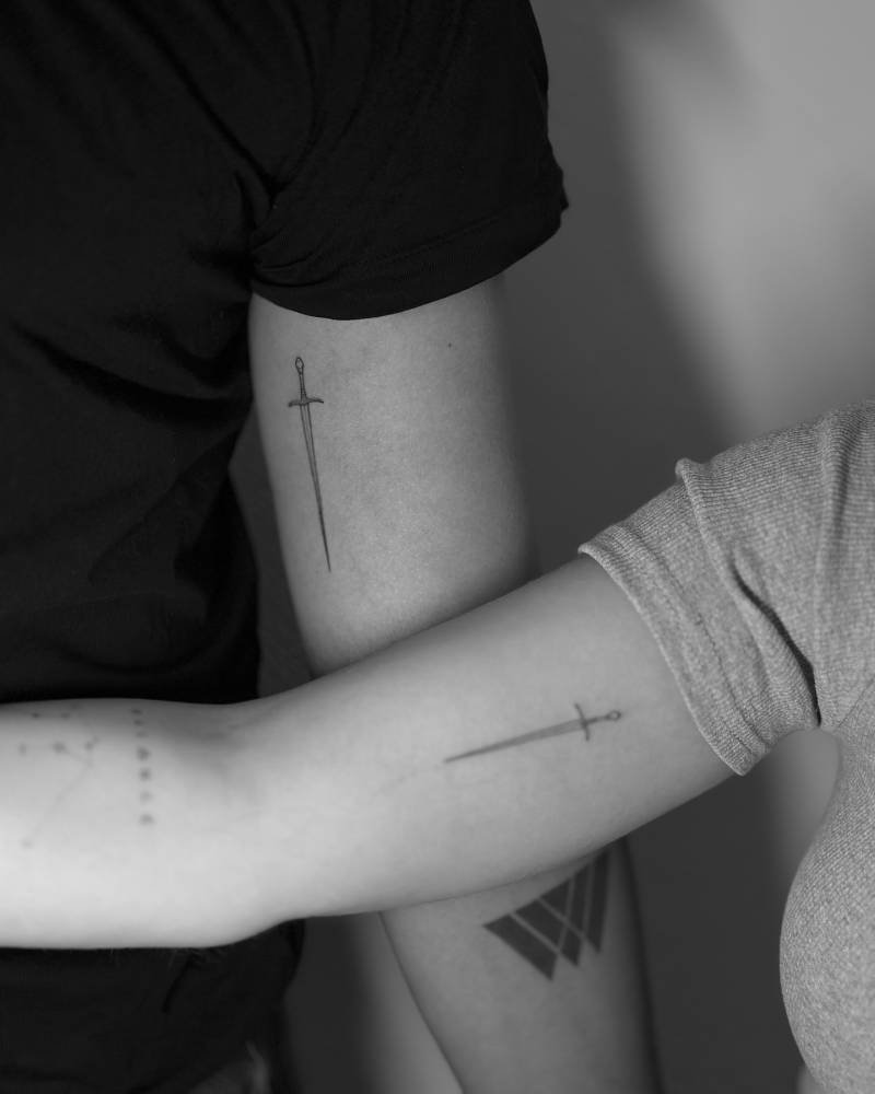 Matching fine line sword tattoo for couple.