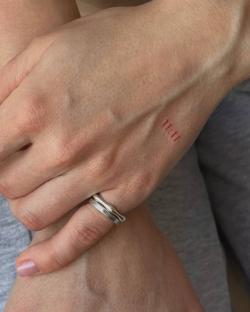 Angel number "11:11" in red ink tattooed on the hand.