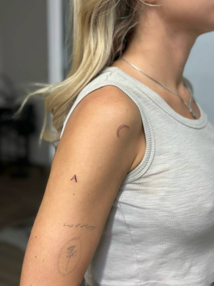 Tiny minimalistic letter "A" tattoo located on the upper arm.