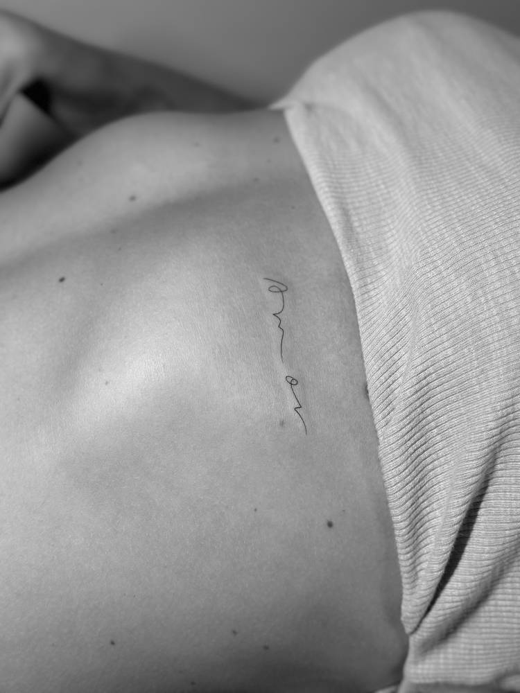 Handwritten font word "amor" tattooed on the rib.