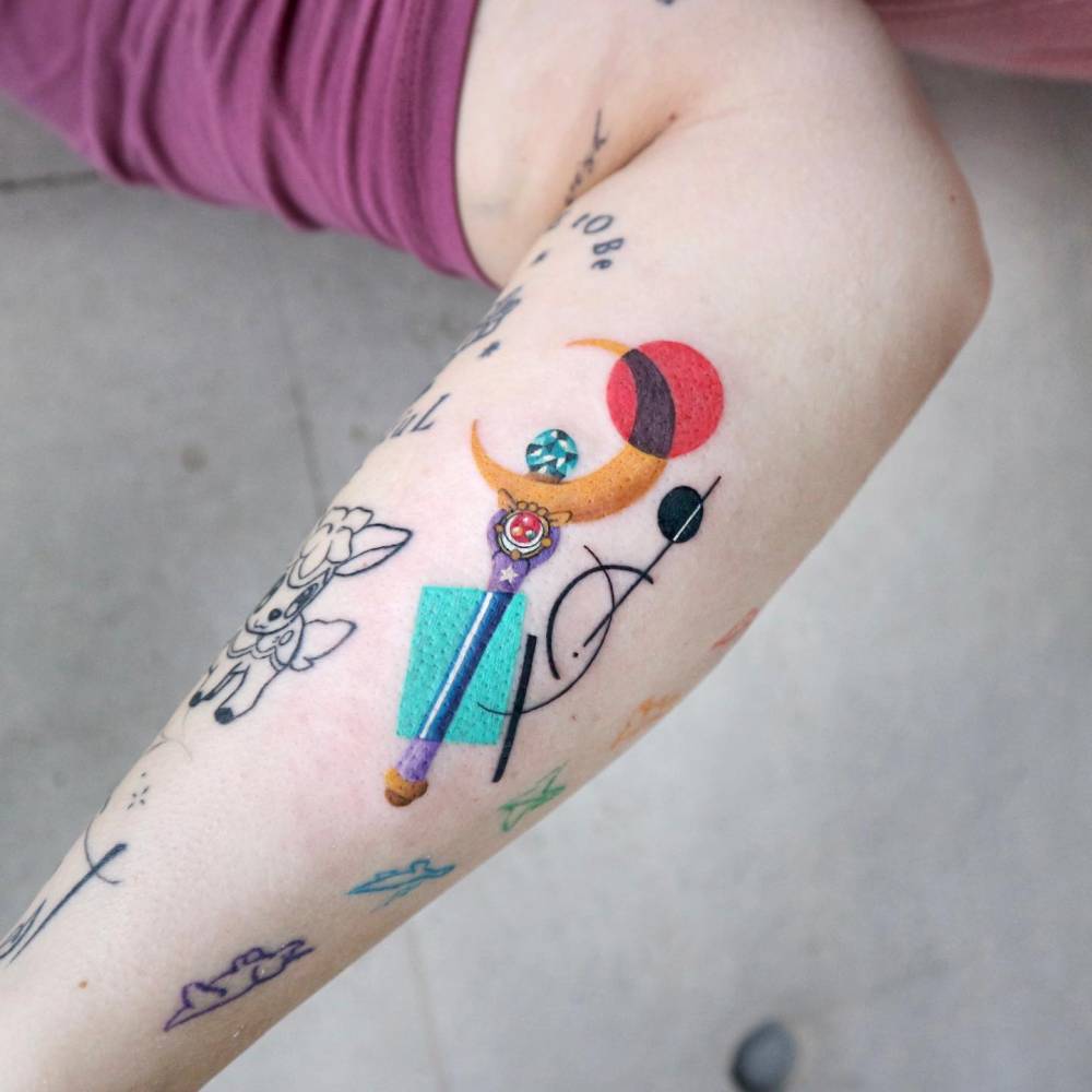 Moon stick tattoo in cartoon style located on the inner forearm.