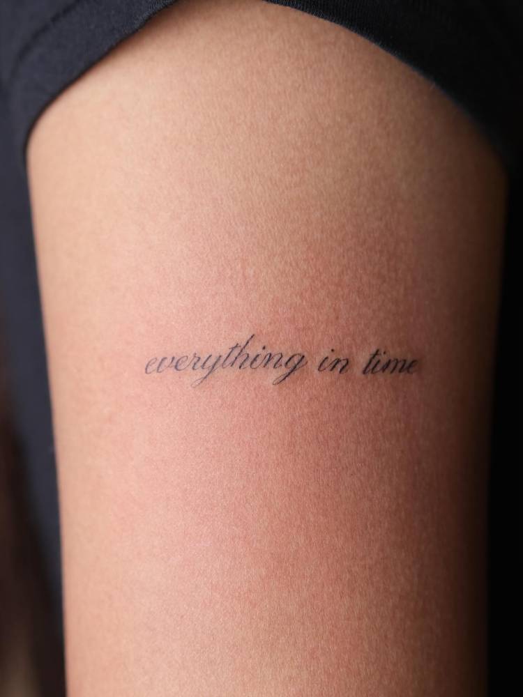 Lettering tattoo that says "everything in time" located on the upper arm.