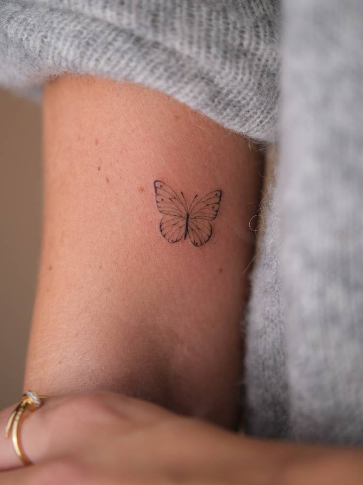 Butterfly tattoo in fine line style located on the bicep.