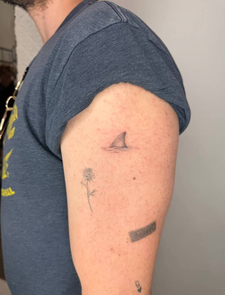 Shark fin tattoo located on the upper arm.