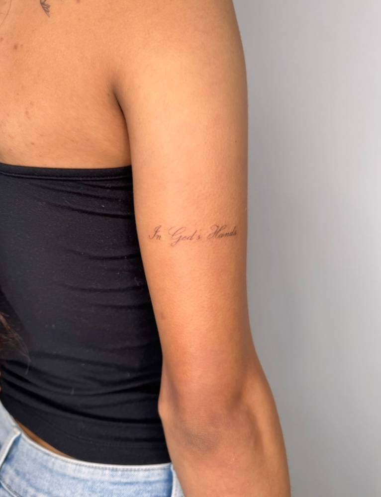 In God's Hands lettering tattoo located on the tricep.