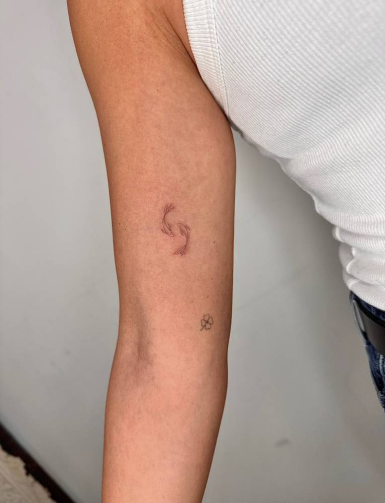 Single needle two opposite fish tattooed on the inner arm.