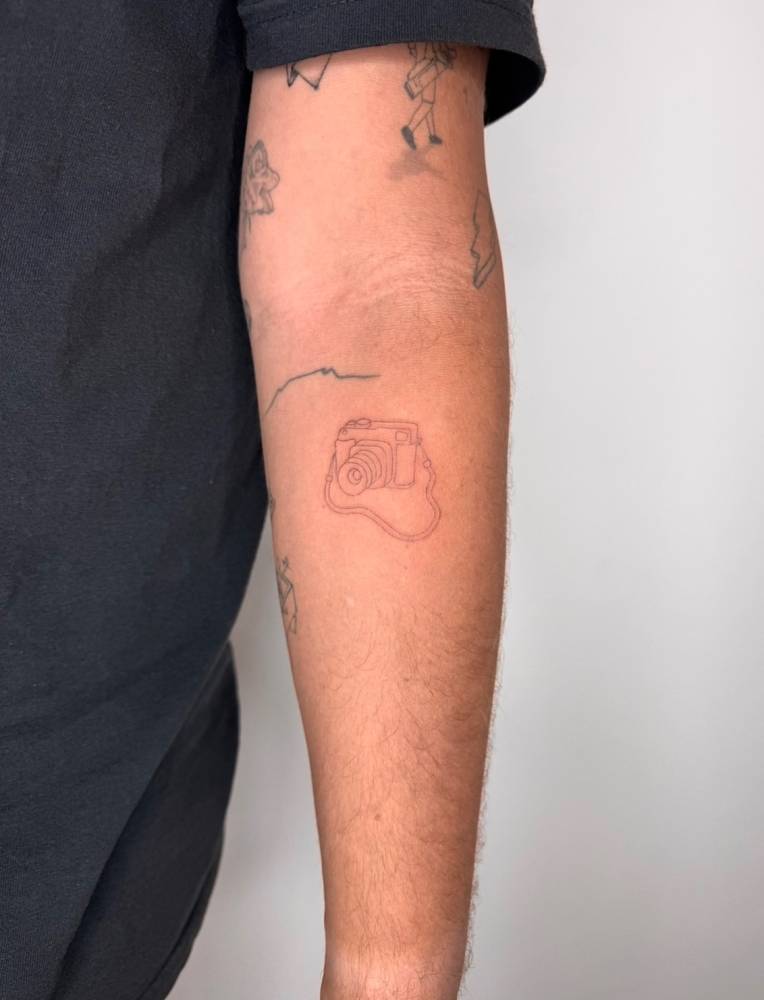 Reflex camera tattoo located on the inner forearm.