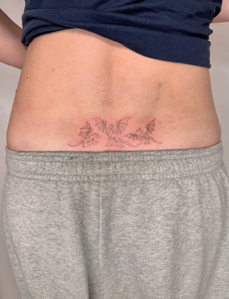 Dragons tattooed on the lower back, done in fine line style.