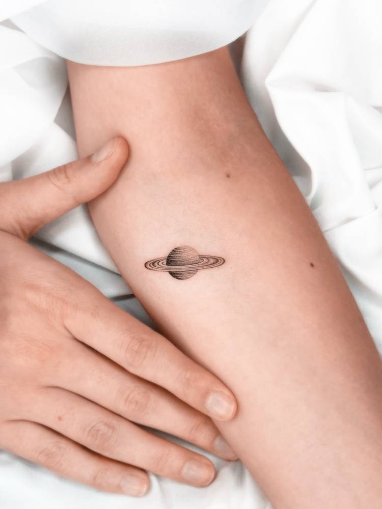 Micro-realistic style Saturn tattoo located on the inner forearm.
