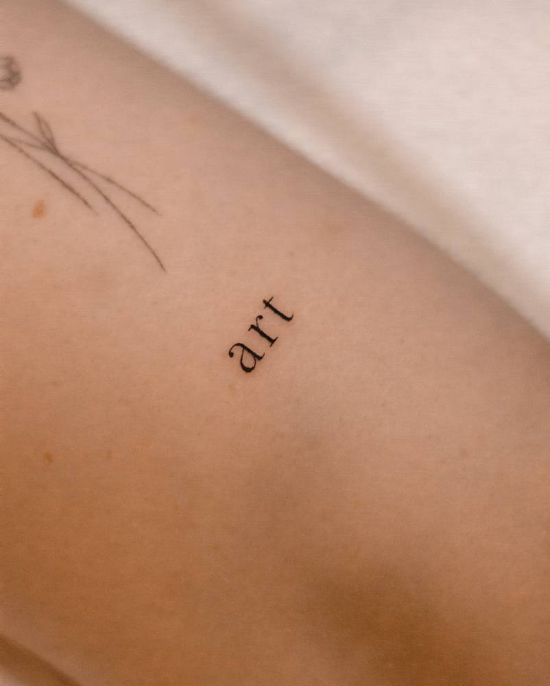 Serif font word "art" tattooed on the tricep.