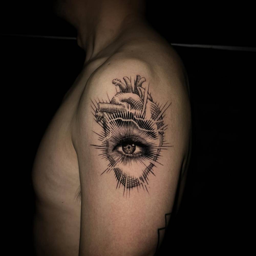 Engraving style eye and anatomical heart tattoo located on the upper arm.