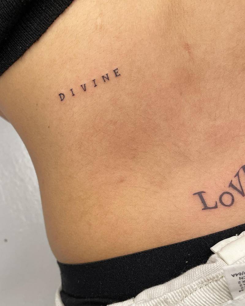 "Divine" lettering tattoo placed on the lower back.